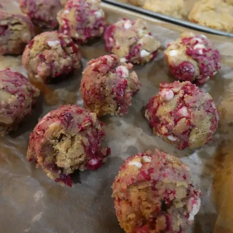 Hand-rolled cookie dough balls flecked with pink berry pieces and white chocolate chips, ready to bake