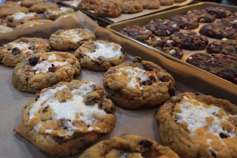 Trays of freshly baked brown butter cookies, including chocolate chip cookies topped with melted marshmallow