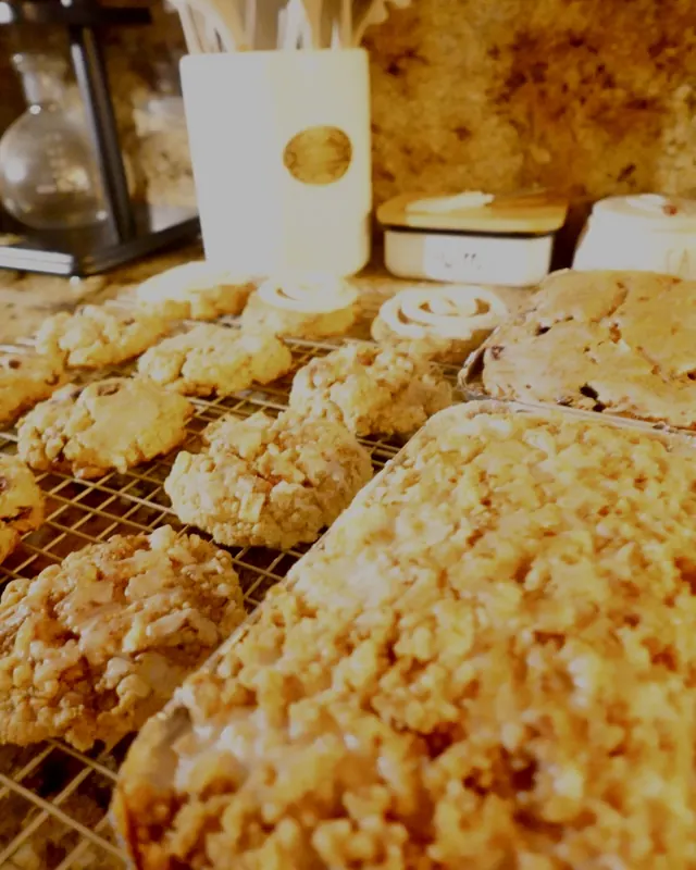 A glazed streusel-topped cake loaf in its baking tin beside cookies on a cooling rack